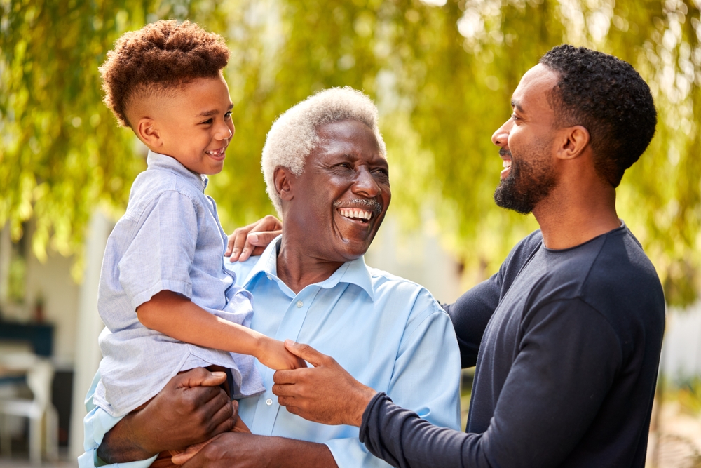 Grandfather with young grandson in arms and smiling at son.