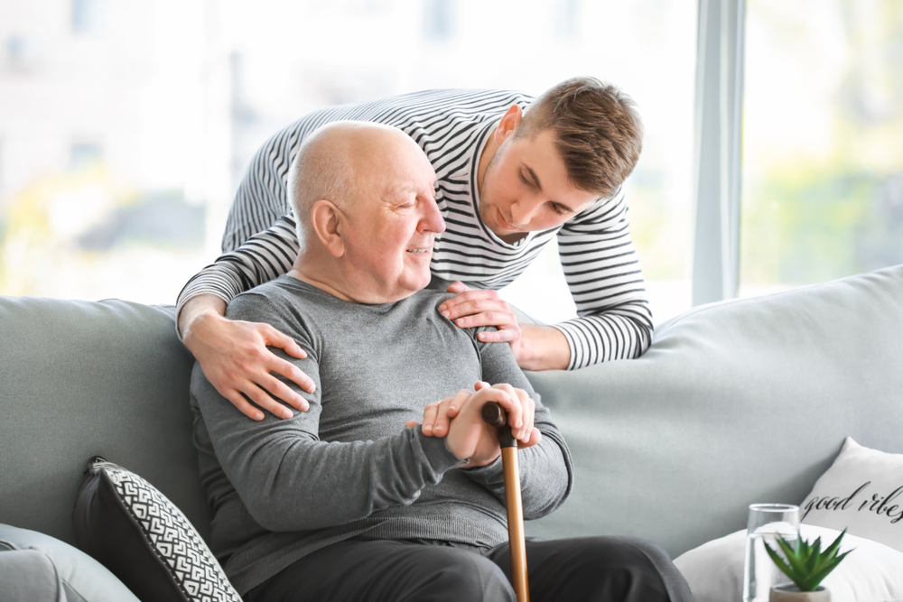 Senior man on couch with cane and adult caregiver looking after him after enjoying short-term stay san juan capistrano